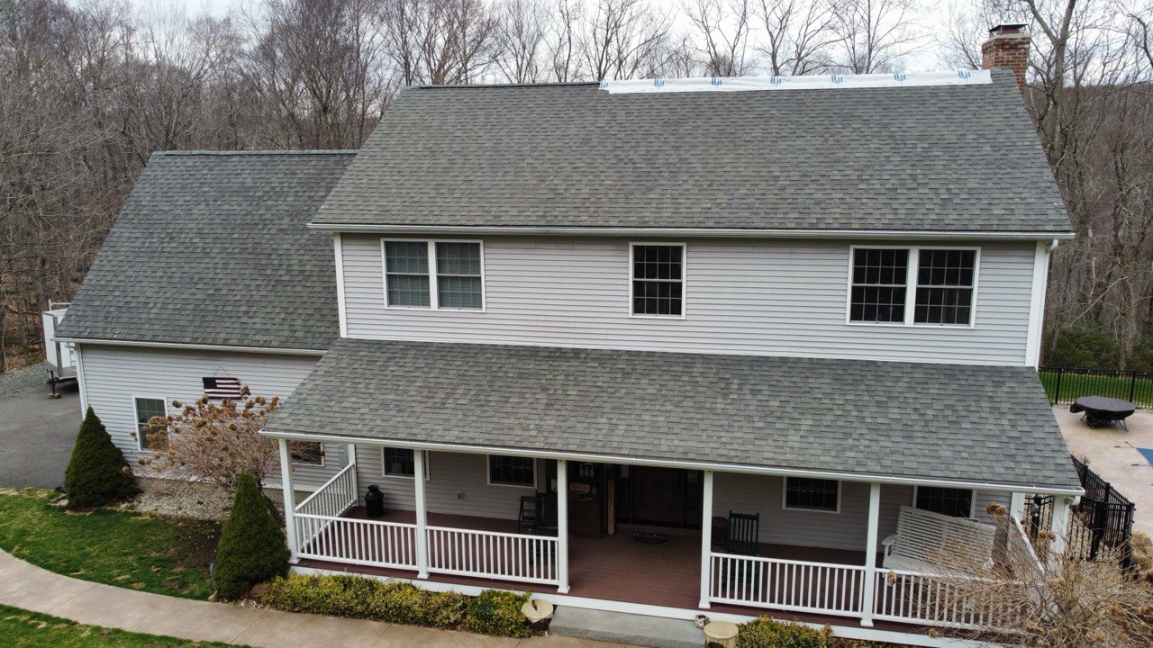 Colonial style house with old white siding, installers standing on the roof